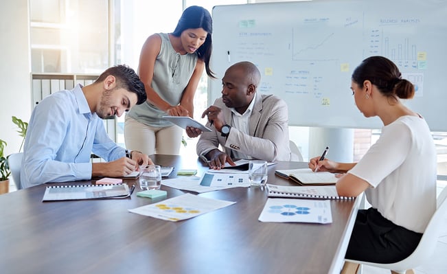 A team of four people discuss and work at a table A team of four people discuss and work at a table