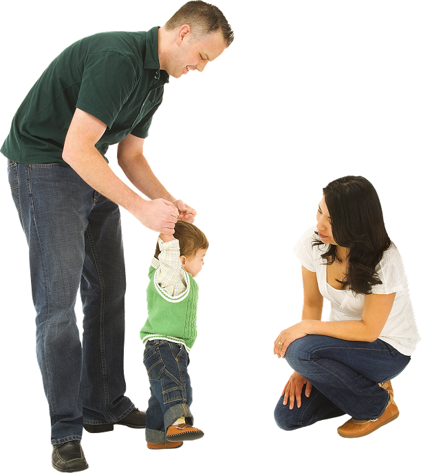 A family of three with the father helping his young child walk