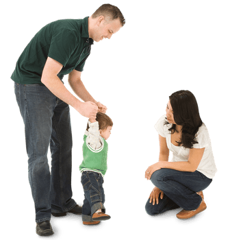 A father helping his young child walk towards the child's mother A father helping his young child walk towards the child's mother