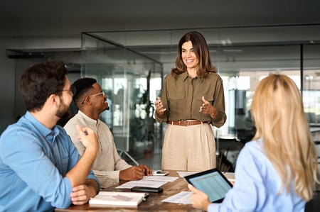 A meeting being led by a woman standing in front of three people