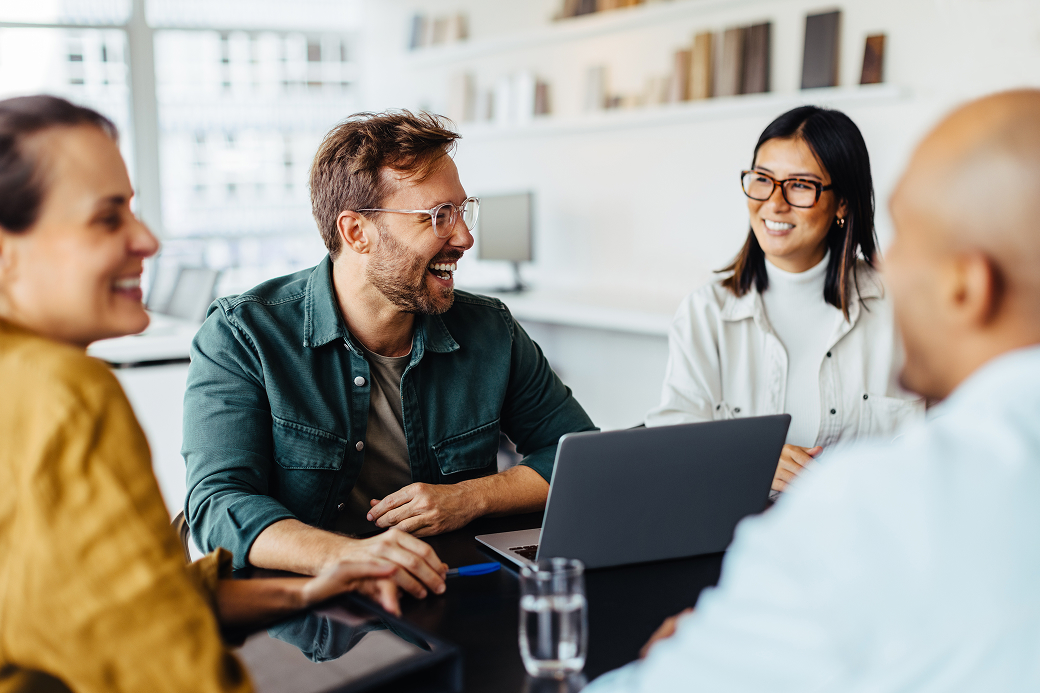 Group of four team members discussing at a table over a laptop Group of four team members discussing at a table over a laptop